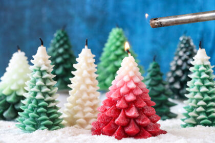 Close-up image of Christmas fir tree forest scene, group of snuffed out Christmas tree wax candles on artificial snow, red candle being relit with safety gas lighter, mottled blue background, focus on foreground