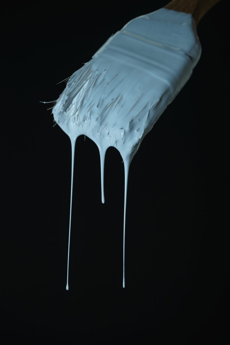Dripping white paint  of old brush on a black background.