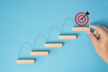 Male hand arranges a wooden block staircase with target icon. Achieving goals and objectives or goal setting